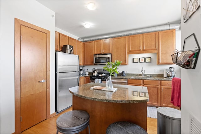 kitchen with appliances with stainless steel finishes, a sink, light wood-style flooring, a kitchen breakfast bar, and a center island