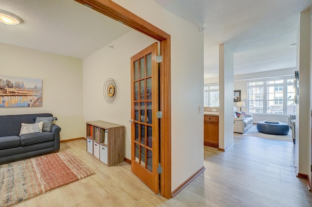 hallway featuring light wood finished floors, baseboards, and a textured ceiling