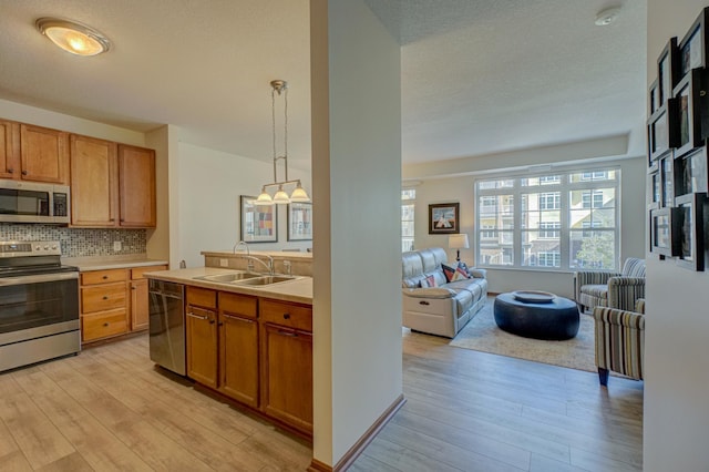 kitchen featuring stainless steel appliances, a sink, open floor plan, light wood finished floors, and decorative backsplash