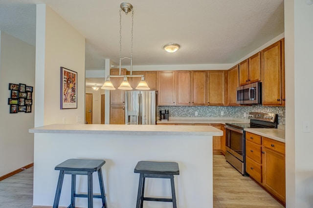 kitchen with stainless steel appliances, a kitchen breakfast bar, light wood-style flooring, light countertops, and tasteful backsplash