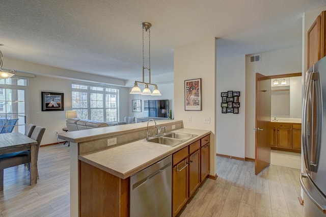 kitchen featuring stainless steel appliances, a sink, open floor plan, brown cabinetry, and light wood-style flooring