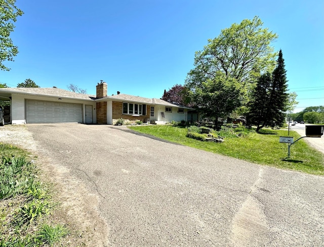 ranch-style house with driveway, a chimney, a garage, a front lawn, and stone siding