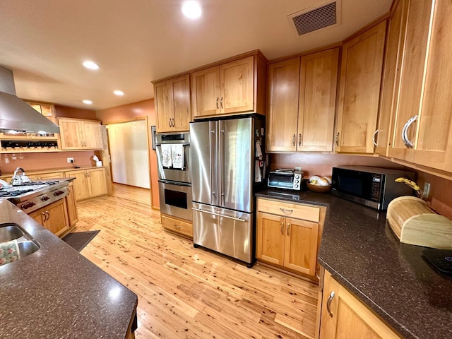 kitchen with appliances with stainless steel finishes, light wood-style floors, ventilation hood, recessed lighting, and dark stone counters