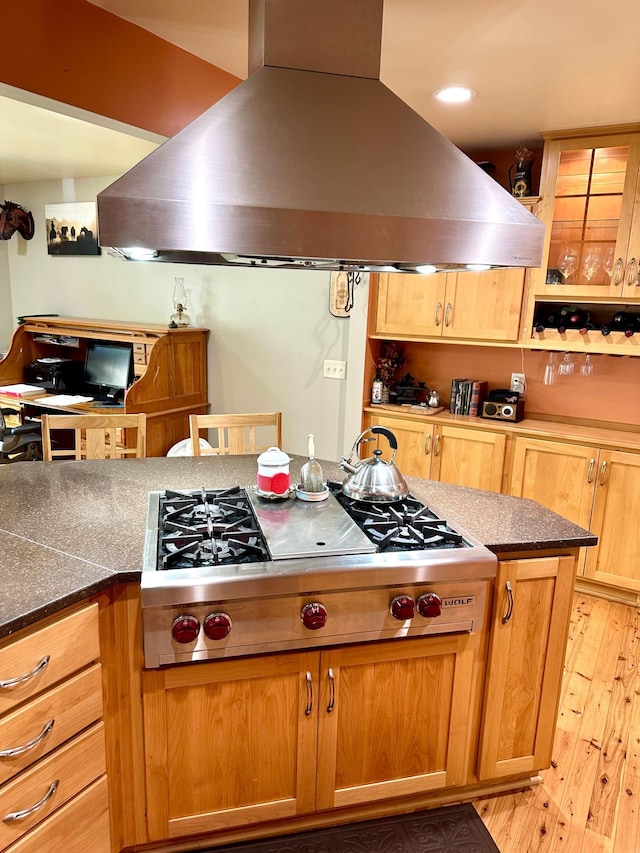 kitchen with island exhaust hood, stainless steel gas cooktop, light wood-style floors, and dark stone counters