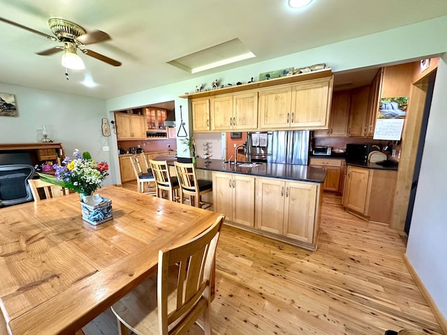 kitchen with a sink, light wood-type flooring, dark countertops, ceiling fan, and stainless steel fridge