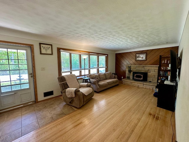 living area featuring a stone fireplace, wooden walls, and a textured ceiling