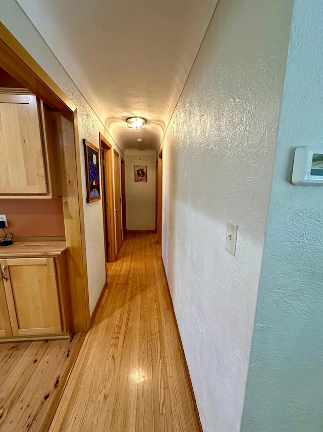 hallway featuring light wood-style floors and a textured wall