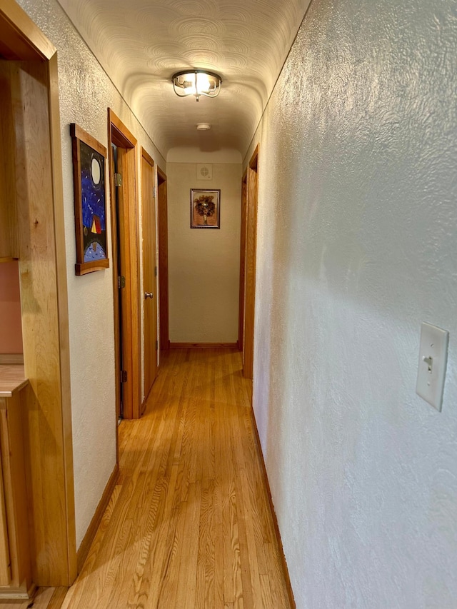hall featuring light wood finished floors and a textured wall