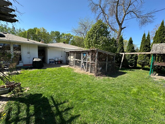 view of green lawn with exterior structure, a patio, an outbuilding, and a playground