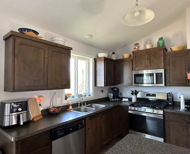 kitchen with stainless steel appliances, dark countertops, a sink, a textured ceiling, and dark brown cabinetry