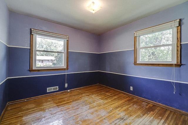 spare room featuring plenty of natural light, wood-type flooring, and baseboards