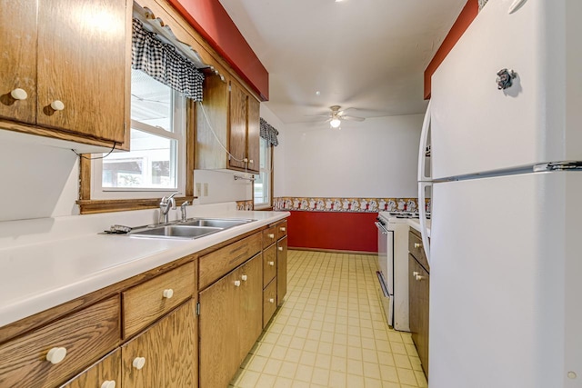 kitchen with white appliances, a sink, light countertops, brown cabinets, and a ceiling fan