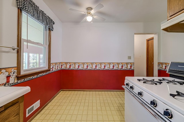 kitchen featuring white gas range oven, ceiling fan, under cabinet range hood, light countertops, and light flooring