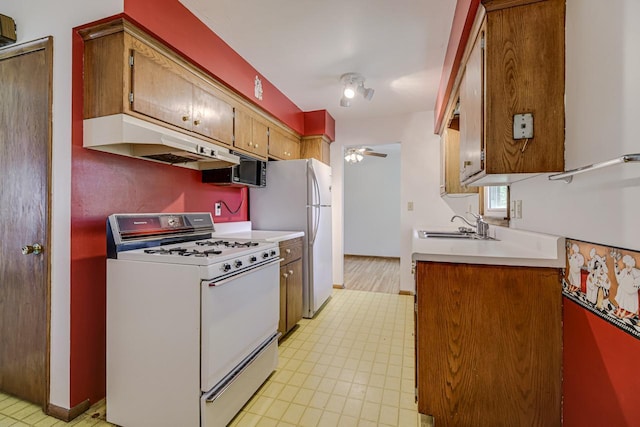 kitchen featuring white appliances, under cabinet range hood, a sink, ceiling fan, and light countertops