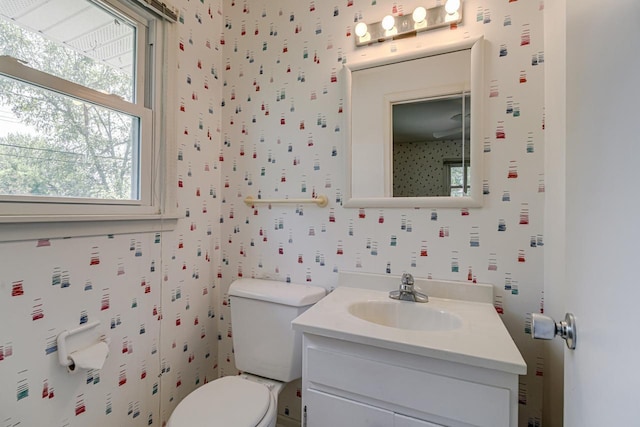 bathroom featuring healthy amount of natural light, vanity, toilet, and wallpapered walls