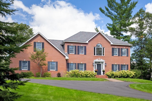 colonial inspired home with brick siding and a front yard