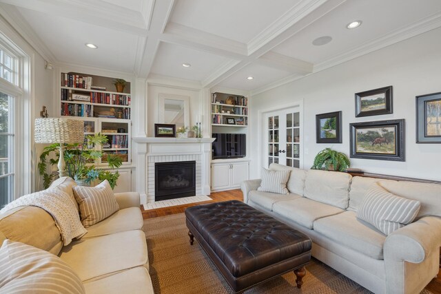living area with beam ceiling, ornamental molding, wood finished floors, a brick fireplace, and built in shelves