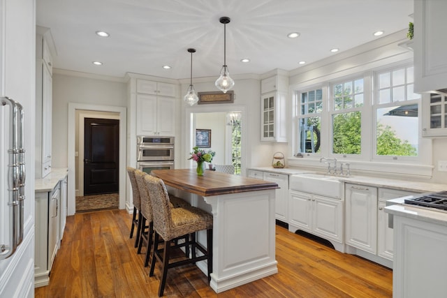 kitchen featuring a sink, butcher block counters, white cabinetry, glass insert cabinets, and stainless steel double oven