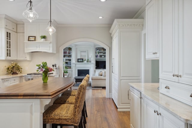 kitchen with recessed lighting, white cabinets, hardwood / wood-style flooring, a kitchen bar, and a brick fireplace