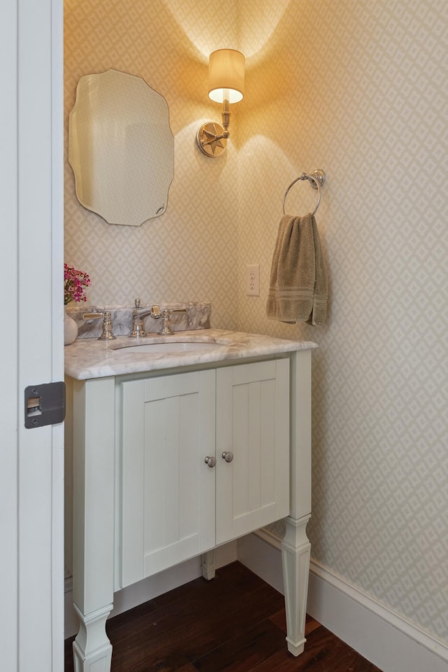 bathroom featuring wallpapered walls, wood finished floors, baseboards, and vanity