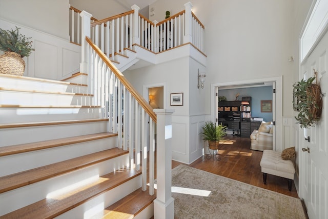 stairs with wood finished floors, a decorative wall, a high ceiling, and wainscoting