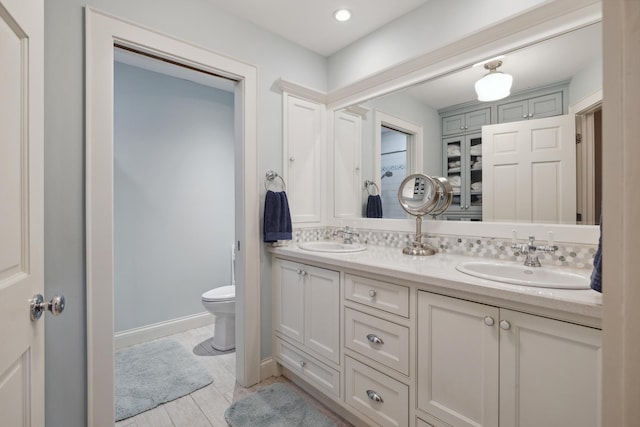 bathroom featuring toilet, double vanity, and baseboards