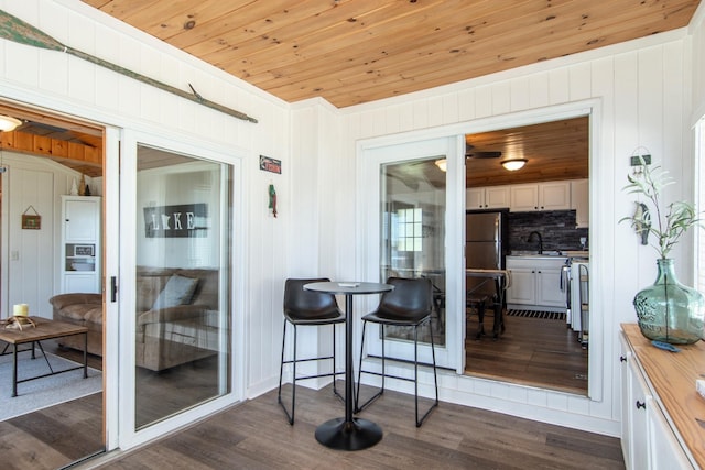 dining space with dark wood-style floors, wooden ceiling, and wooden walls