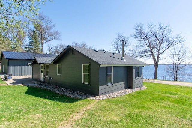 view of side of property with a yard, a shingled roof, and a water view