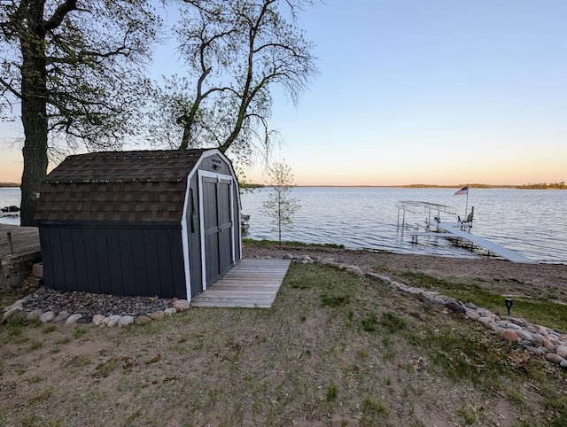 outdoor structure at dusk featuring a storage shed, a water view, and an outbuilding
