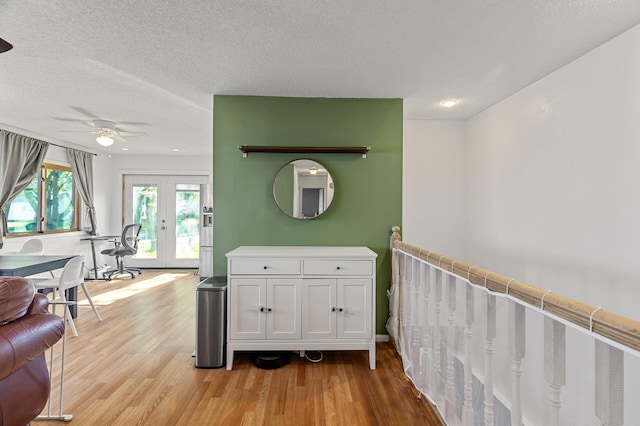corridor featuring french doors, light wood-style floors, and a textured ceiling