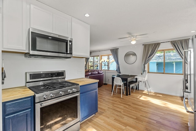 kitchen with stainless steel appliances, wood counters, blue cabinetry, white cabinetry, and a ceiling fan