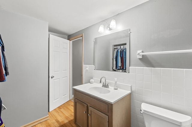 bathroom with toilet, wood finished floors, vanity, a closet, and tile walls
