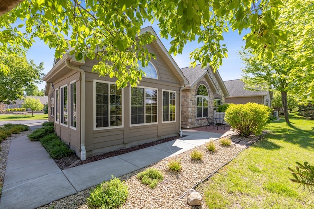 24107 Rivers Edge Rd, Rogers, MN 55374 - view of home's exterior featuring stone siding, a patio area, a lawn, and roof with shingles