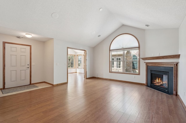 24107 Rivers Edge Rd, Rogers, MN 55374 - unfurnished living room featuring a fireplace with flush hearth, plenty of natural light, a textured ceiling, vaulted ceiling, and wood finished floors