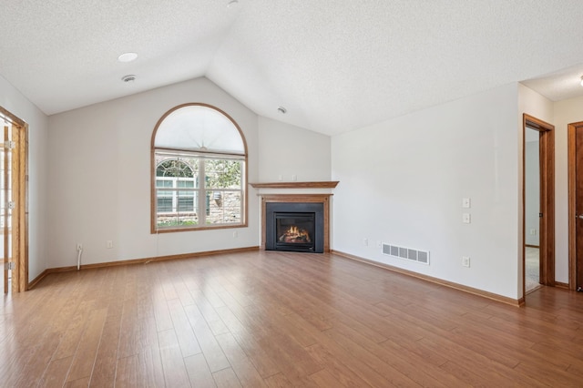 24107 Rivers Edge Rd, Rogers, MN 55374 - unfurnished living room with a textured ceiling, vaulted ceiling, a glass covered fireplace, wood finished floors, and baseboards