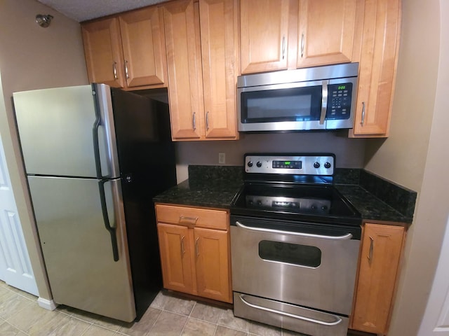 kitchen featuring appliances with stainless steel finishes, dark stone counters, and light tile patterned floors