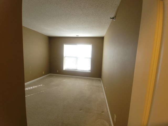 spare room with a textured ceiling, carpet flooring, and baseboards