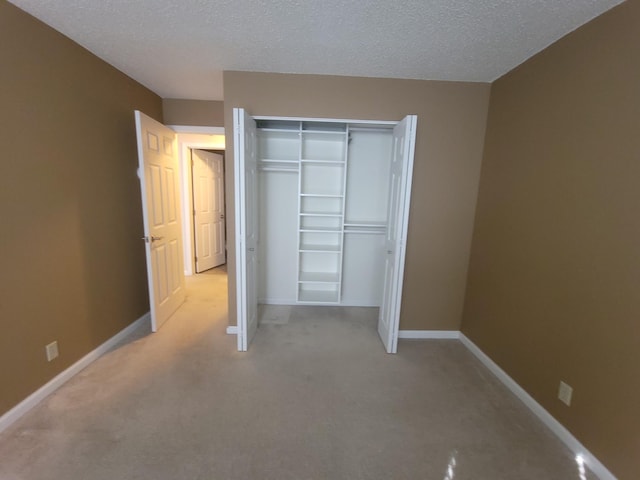unfurnished bedroom with light colored carpet, baseboards, a textured ceiling, and a closet
