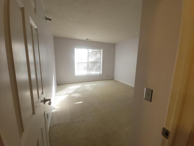 spare room featuring light colored carpet and a textured ceiling