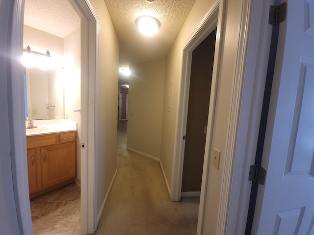 hallway featuring a textured ceiling, a sink, and baseboards