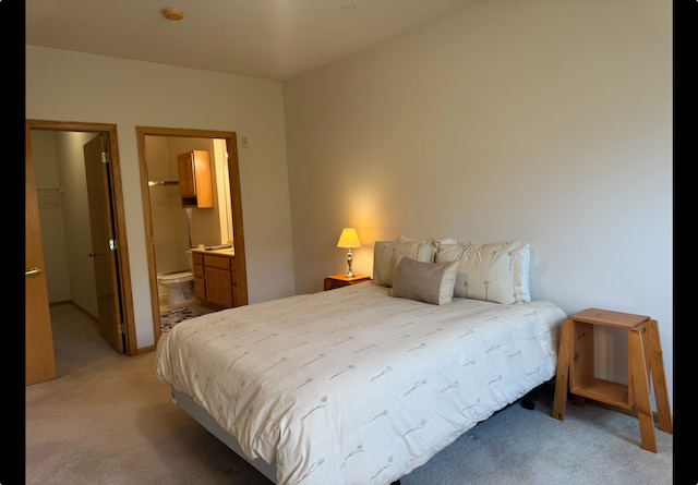 bedroom with light colored carpet, ensuite bathroom, and a walk in closet