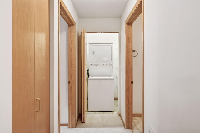 hall featuring stacked washing machine and dryer, light carpet, and baseboards