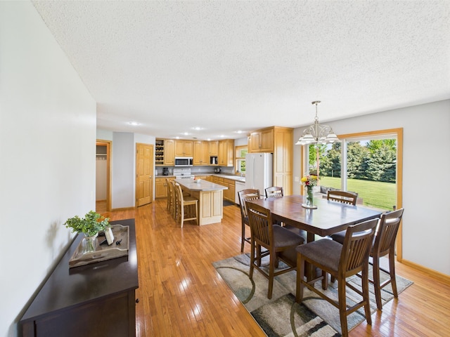 dining room with a textured ceiling, a chandelier, light wood finished floors, and baseboards
