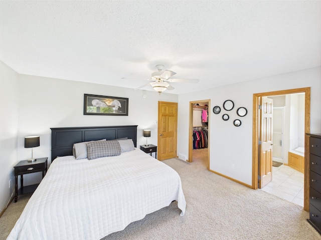 bedroom featuring a walk in closet, baseboards, a closet, light carpet, and a ceiling fan