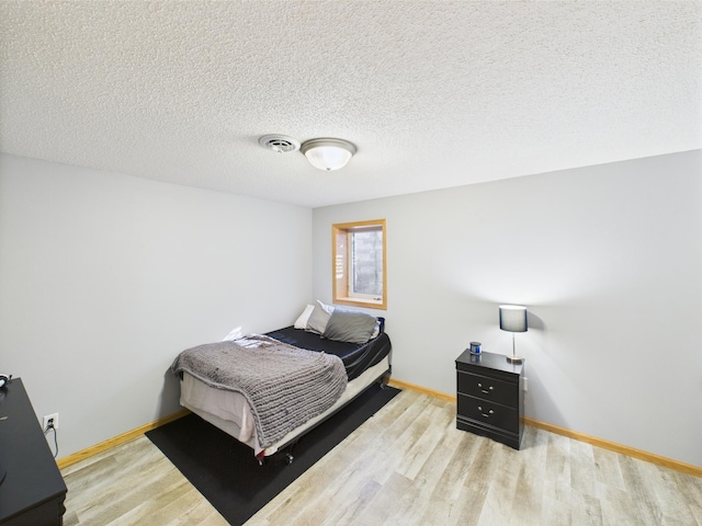 bedroom with wood finished floors, baseboards, and a textured ceiling