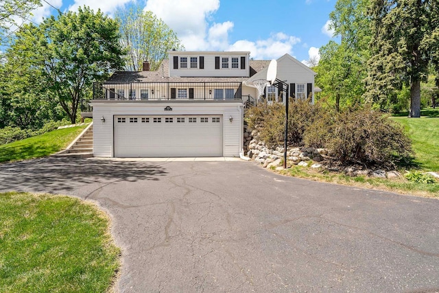 traditional-style house featuring a balcony, asphalt driveway, a garage, a chimney, and stairway