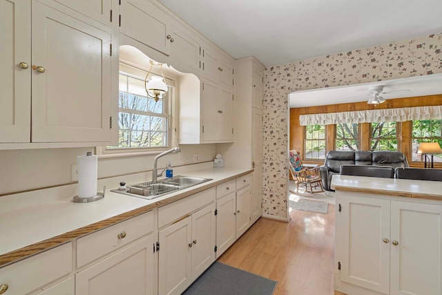 kitchen with a sink, light wood-style flooring, wallpapered walls, white cabinetry, and light countertops