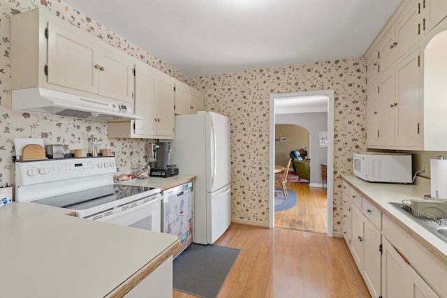 kitchen with white appliances, under cabinet range hood, wallpapered walls, light wood-style floors, and light countertops