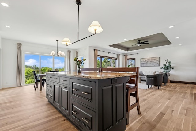 2169 Ibson Ave SE, Rockford Twp, MN 55313 - kitchen with light wood finished floors, a kitchen bar, a tray ceiling, a chandelier, and a kitchen island