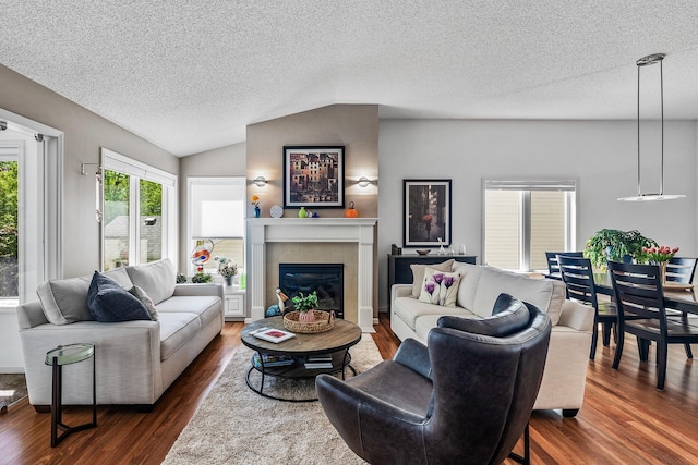 living room featuring dark wood-style flooring, a textured ceiling, lofted ceiling, and a tiled fireplace